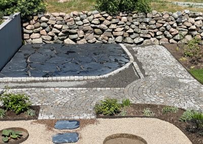 En trädgård med stenmur med olika former och storlekar av gatsten och skiffer lagda i olika mönster